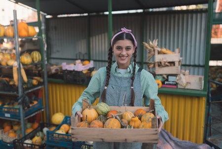 Farmer woman holds a wooden box with pumpkins in handsの写真素材