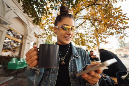 Woman sitting outdoors cafe drinking beverage holding in hand smartphone