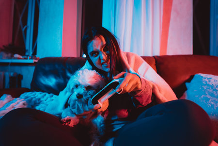 Close up portrait of A gamer or a streamer girl at home in a dark room with a game controller playing with her dog and sits in front of a monitor or TV.の写真素材