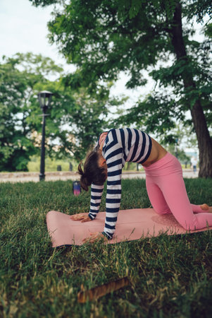 At the park yoga class, a sporty girl is engaging in stretching exercises.