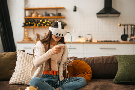 Amidst a cozy Christmas scene at home, a trendy young lady enjoys a virtual reality headset.の写真素材