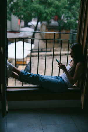 A young woman enjoying a moment of relaxation on her balcony while using a smartphoneの写真素材