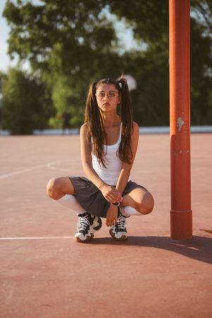 A girl squats on a basketball court, basking in the warm sunlight, radiating joyの写真素材