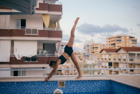 A highly skilled gymnast executes a truly impressive handstand at the poolside during duskの写真素材