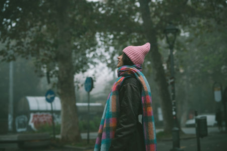 Woman in a pink hat and scarf walks down a foggy streetの写真素材
