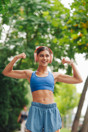 A confident and empowered woman is exercising outdoors, wearing headphones and smiling widelyの写真素材