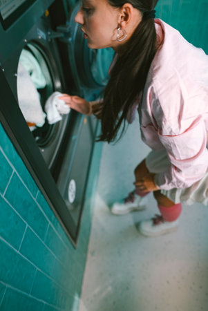 A young woman happily doing laundry in a chic, vibrant laundromat filled with modern appliancesの写真素材