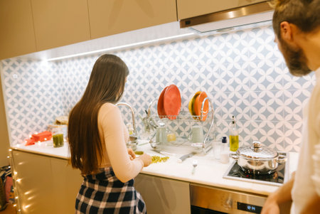A Cozy Kitchen Scene Featuring a Cooking Couple Engaged in Delicious Meal Preparationの写真素材