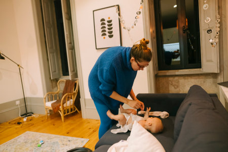 A caring mother lovingly changes her babys diaper in the warm and cozy living room environmentの写真素材