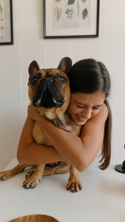 A woman joyfully embracing her adorable French Bulldog in a cozy, warm setting at homeの写真素材