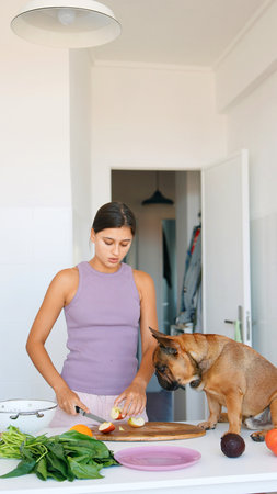 A woman happily cooking alongside her dog in a modern and vibrant kitchen settingの写真素材