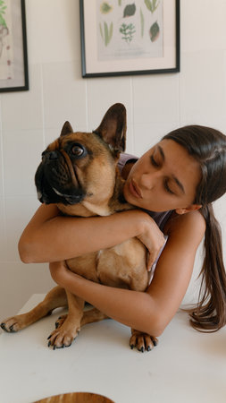 A woman is cuddling her French Bulldog in a cozy indoor setting, filled with warmth and comfortの写真素材