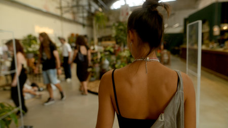 A stylish woman strolls through a trendy venue, enjoying lush greenery and the atmosphere
