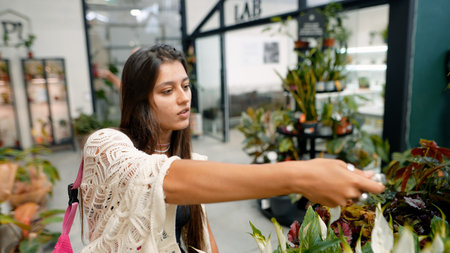 A Young Woman Happily Choosing and Selecting Various Plants in a Modern Greenhouse Environmentの写真素材