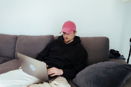 Young man concentrating on laptop in peaceful apartment settingの写真素材