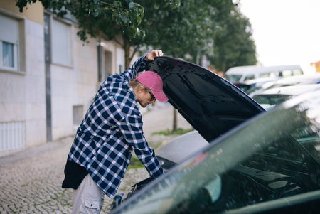 Young man diagnosing car engine on residential street during daytimeの写真素材