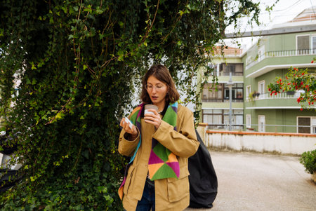 Young woman with backpack drinking coffee outdoors smiling warmlyの写真素材