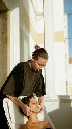 Black client receiving facial from white aesthetician on sunlit balcony