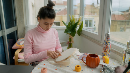 Focused woman crafting intricate embroidery under daylight