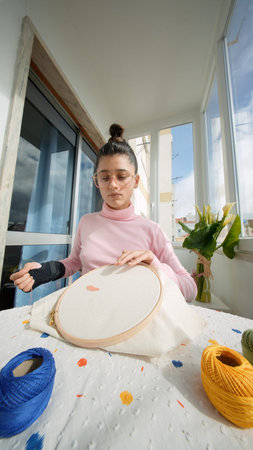Woman stands proudly by window with vibrant embroidery on display