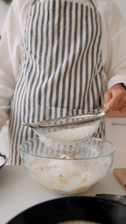Calm kitchen scene with flour softly pouring through sieve into dishの写真素材