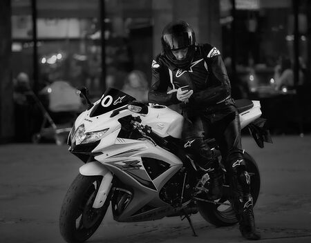 10-07-2018 Riga, Latvia. Motorcyclist in black full suit near motorcycle reading messages in phone....