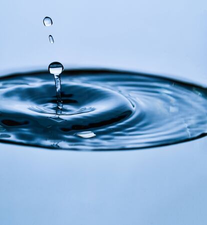 A bubble splash of transparent clear water liquid in glass on a light blue background at sunlight.の写真素材