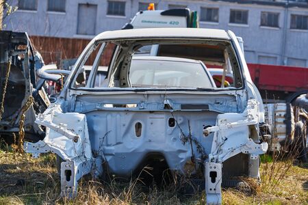 old gray car frame disassembled car with rusty parts on the street near the fence.