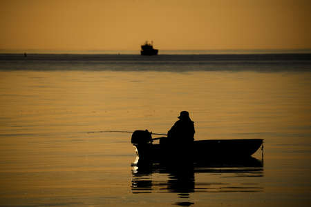 Latvia Fishing boat and fisherman in sea at dawn.