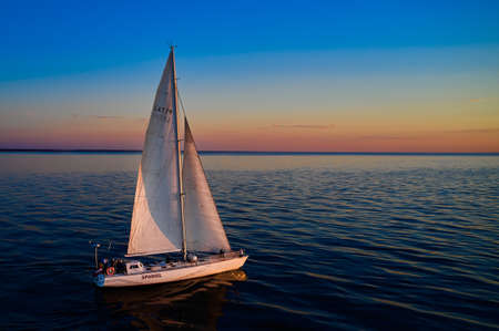 Riga, Latvia 12-06-2021 Yacht sailing against sunset. Holiday lifestyle landscape with skyline sailboat. Yachting tourism - maritime evening walk. Romantic trip on luxury yacht during the sea sunset.のeditorial素材