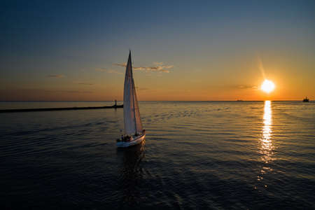 Riga, Latvia 12-06-2021 Yacht sailing against sunset. Holiday lifestyle landscape with skyline sailboat. Yachting tourism - maritime evening walk. Romantic trip on luxury yacht during the sea sunset.のeditorial素材