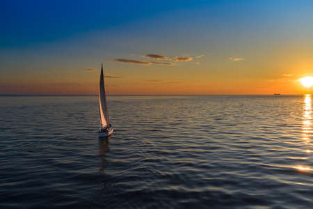 Riga, Latvia 12-06-2021 Yacht sailing against sunset. Holiday lifestyle landscape with skyline sailboat. Yachting tourism - maritime evening walk. Romantic trip on luxury yacht during the sea sunset.のeditorial素材