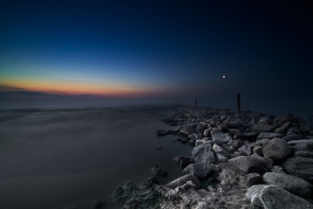 A long exposure shot of a rocky beach at night with a moon in the skyの写真素材