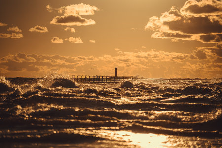 Baltic sea at sunset. Dramatic sky, glowing clouds, waves and pierの写真素材