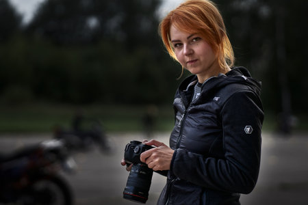 Young red-haired female photographer in a black jacket and jeans with a camera in her hands.のeditorial素材