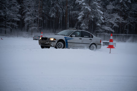 12-12-2022 Riga, Latvia a car driving through a snow covered forest area with a red and white traffic cone in the foreground. .のeditorial素材