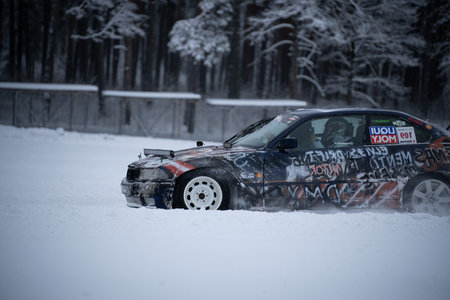 12-12-2022 Riga, Latvia a car covered in graffiti driving through the snow in a parking lot with trees in the background and a fence in the foreground. .のeditorial素材