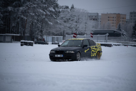 12-12-2022 Riga, Latvia a car is driving through the snow in a city park with trees and buildings in the background and a flag pole sticking out of the car. .のeditorial素材