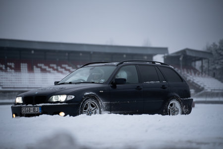 12-12-2022 Riga, Latvia a black car parked in the snow near a stadium area with a building in the background and a snow covered field. .のeditorial素材