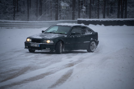 12-12-2022 Riga, Latvia a car is driving through the snow in the woods on a road that is covered in snow and has a few trees. .のeditorial素材