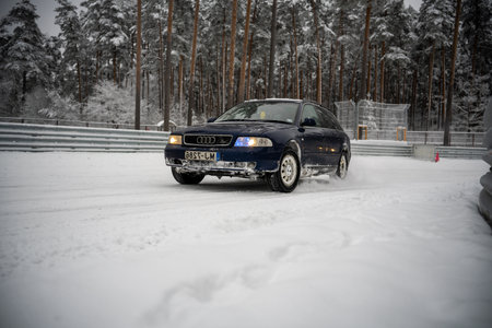 12-12-2022 Riga, Latvia a car driving through the snow in front of a forest of trees and a fence with a fence in the background. .のeditorial素材