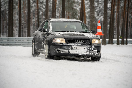 12-12-2022 Riga, Latvia a car is driving through a snowy road with a traffic cone in the background and trees in the background. .のeditorial素材