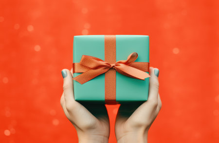 Female hands holding a gift box with a bow on a red backgroundの素材