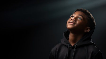 Young african american woman in hoodie looking up on black backgroundの素材
