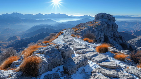 a view from the top of a mountain with snow on the ground and grass in the foreground, with a bright sun in the sky above the mountain range. .の素材