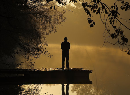 Silhouette of a man standing on the edge of a lake.の素材