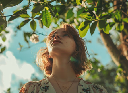 Beautiful young woman with red hair and green leaves on sunny dayの素材