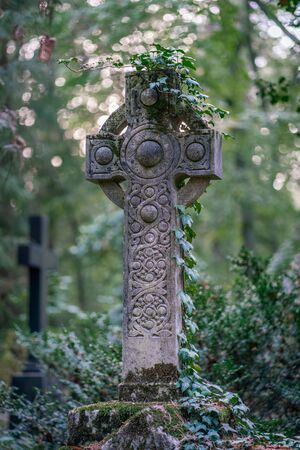 Celtic stone cross monument covered with ivy on a graveyard in a forest