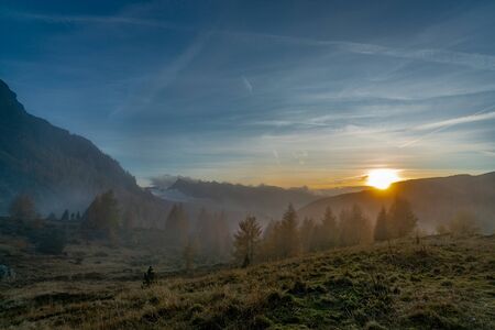 Sunset on a foggy autumn evening overlooking the valley at the Valles pass in the italian Dolomites