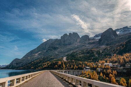 Street on top of the Fedaia reservoir dam at the foot of the Marmolada mountains in South Tyrol on a sunny and clear autumn dayの写真素材